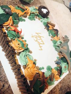 a birthday cake decorated with leaves and other decorations on a counter top in the shape of an oval