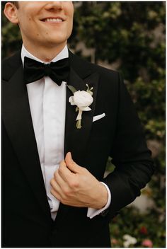 a man in a tuxedo smiles while wearing a white rose boutonniere