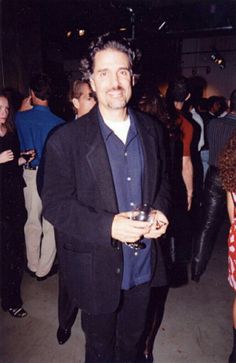 a man in a suit and tie holding a wine glass at a party with other people