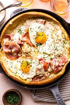 an omelet with bacon and eggs in a skillet next to glasses of orange juice