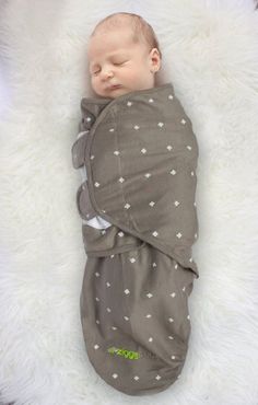 a newborn baby wrapped in a blanket on top of a fluffy white rug, sleeping