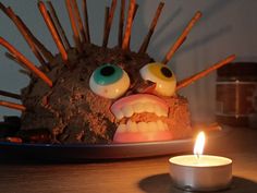 a lit candle sitting on top of a table next to a cake with an evil face