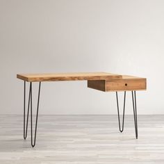 a wooden desk with hairpin legs and a drawer on the top, in front of a white wall