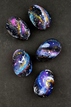 four painted rocks sitting next to each other on a black surface with space in them