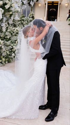 a bride and groom kissing in front of a wedding arch with white flowers on it