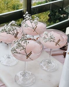 four martini glasses with flowers in them sitting on a white counter top next to a window