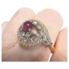 This Art Deco-style ring from the 1920-1925 period is crafted in 18K gold with platinum accents and features Diamonds and a ruby cabochon. It has a weight of 4.12 grams and is sized 15.5/55.5. The Diamonds are simple-cut, totaling 0.90 carats, and are of SI-VS clarity and H-G color grade. The other gemstone is a ruby cabochon weighing 0.80 carats. The ring measures 2.2 cm in length and 1.5 cm in width. The gemstones are set in claw settings. **IN STOCK** Characteristics: Material: 18K Gold with Art Deco Diamond Cabochon Rings, Art Deco Diamond Rings With Cabochon, Vintage Ruby Ring With Rose Cut Diamonds, Antique Diamond Cabochon Rings, Antique Ruby Cabochon Ring, Heirloom Yellow Gold Cabochon Ruby Ring, Antique Ruby Diamond Ring Hallmarked, Vintage Diamond Cabochon Rings, Victorian Cabochon Ruby Ring For Anniversary