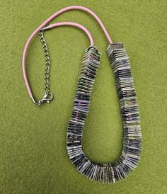 a necklace made out of newspaper strips on a green surface with a pink cord attached to it