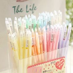 there are many pens in the holder on the table and one is pink, yellow, green, blue