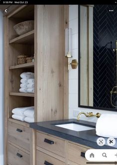 a bathroom with wooden cabinets and black counter tops, gold faucet, white towels