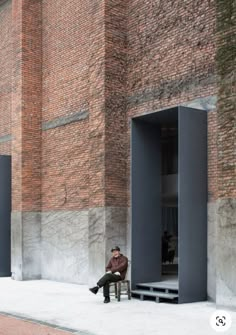 a man sitting on a bench in front of a brick building with two open doors