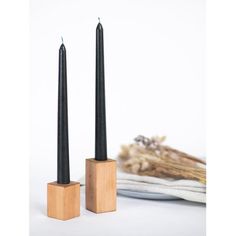 two black candles sitting next to each other on top of a white plate and wooden block