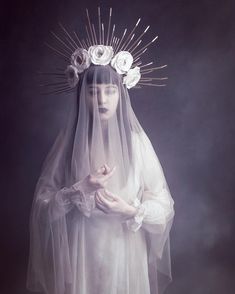 a woman wearing a veil with flowers on her head and hands in front of her face