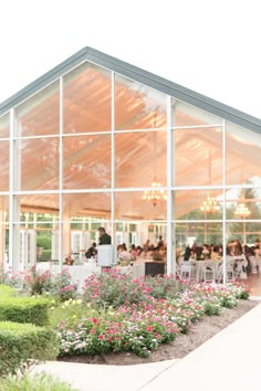 an outdoor dining area with flowers and greenery in the foreground, surrounded by glass walls