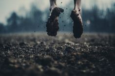 a person jumping in the air with their feet up and dirt on the ground behind them