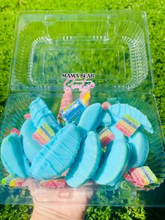 a person holding up a plastic container filled with blue and pink donuts in front of green grass