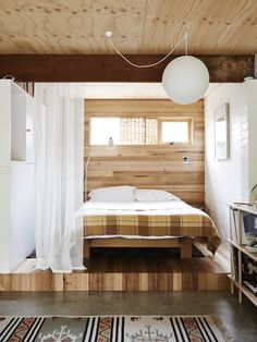 a bedroom with wood paneling and white curtains on the window sill, along with a bed that has a checkered bedspread