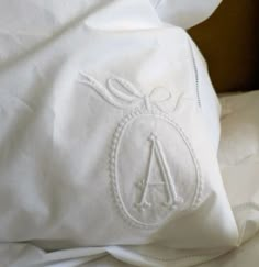 an embroidered pillow on top of a bed with white sheets and pillows in the background