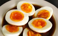 four hard boiled eggs sitting on top of a white plate filled with brown liquid and sauce