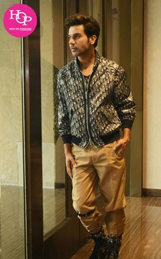 a man standing in front of a glass door wearing brown pants and a patterned shirt