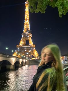 a woman standing in front of the eiffel tower at night with her hair blowing in the wind