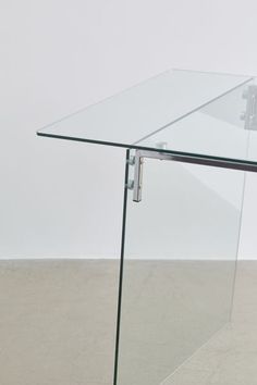 a glass table with metal legs on concrete flooring and white wall in the background