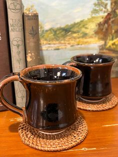 two coffee mugs sitting on top of a wooden table next to an old book