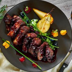 a plate with meat, fruit and vegetables on it next to a knife and fork