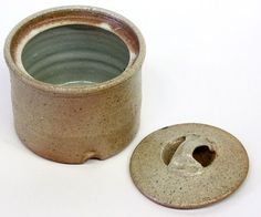 a ceramic cup with a hole in the middle next to a small round object on a white surface