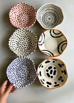 four bowls with different designs on them are being held by a person's hand