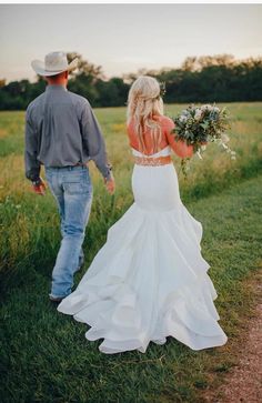 a bride and groom walking through the grass holding hands in front of an open field