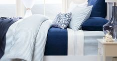 a bed with blue and white comforters in a bedroom next to a lamp on a table