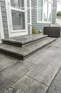 two steps leading up to the front door of a house with gray siding and white trim