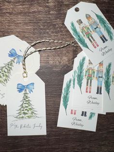 four christmas tags with watercolors on them sitting on a wooden table next to twine string