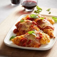 chicken parmesan with tomato sauce and basil on a white platter next to a glass of red wine