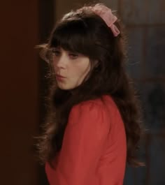 a woman with long dark hair wearing a red shirt and pink bow in her hair