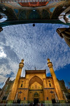 an ornate building with many arches and pillars in front of it, under a cloudy blue sky