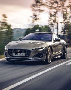 a silver sports car driving down the road with trees in the backgrouund