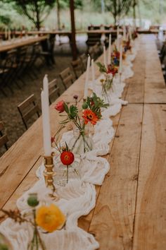 a long wooden table with candles and flowers on it, set up for an outdoor dinner