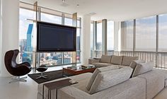 a living room filled with furniture next to tall windows and a flat screen tv mounted on the wall