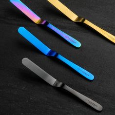 three different colored knives on a black surface