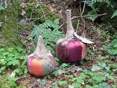 two painted pumpkins sitting on the ground next to green plants and trees with leaves around them