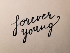 the word forever young written in black ink on white paper with handwritten lettering below it