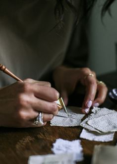 a woman is working on some paper with a pen and scissors in her hand while sitting at a table