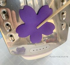 a purple flower with two wooden sticks sticking out of it's center, sitting on top of a metal object