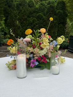 two vases filled with flowers sitting on top of a white tablecloth covered table