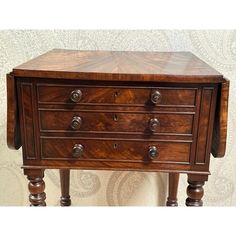 an antique chest of drawers with wooden legs and knobs on the top, against a wallpapered background