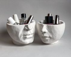 two white ceramic faces with pens and lipstick in them