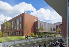 people are sitting on benches in front of a brick building with many windows and grass