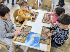 three children sitting at a table playing with sand and sea creatures in wooden trays